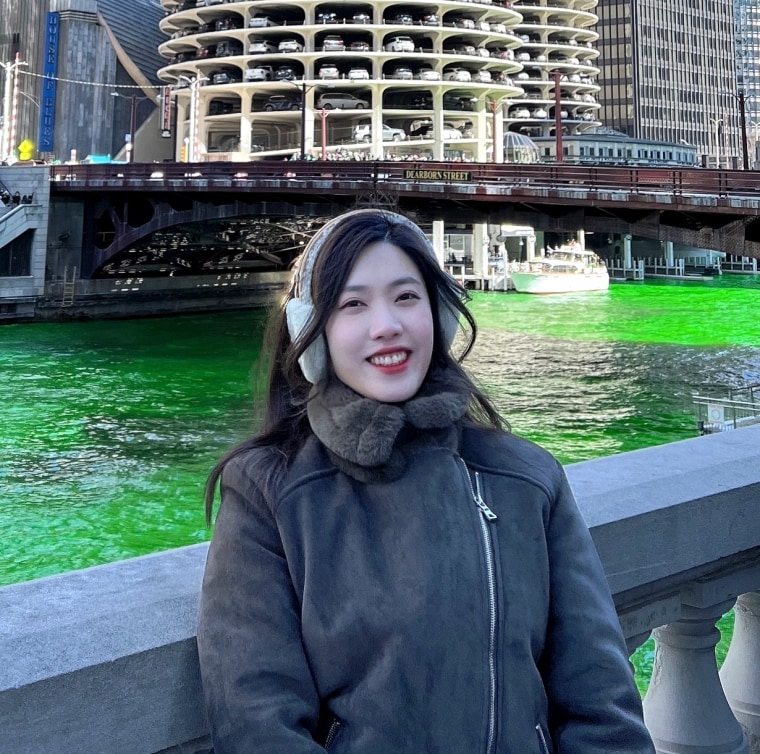 Jieun Kim, standing beside the Chicago River, which looks like it has been dyed green for St. Patrick's Day, with the Marina Towers behind her