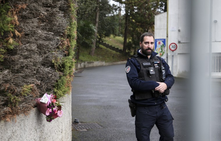 A police officer guards the entrance to a private Catholic school next to a bouquet of flowers after a teacher was stabbed to death by a student on Feb. 22, 2023 in Saint-Jean-de-Luz, France.