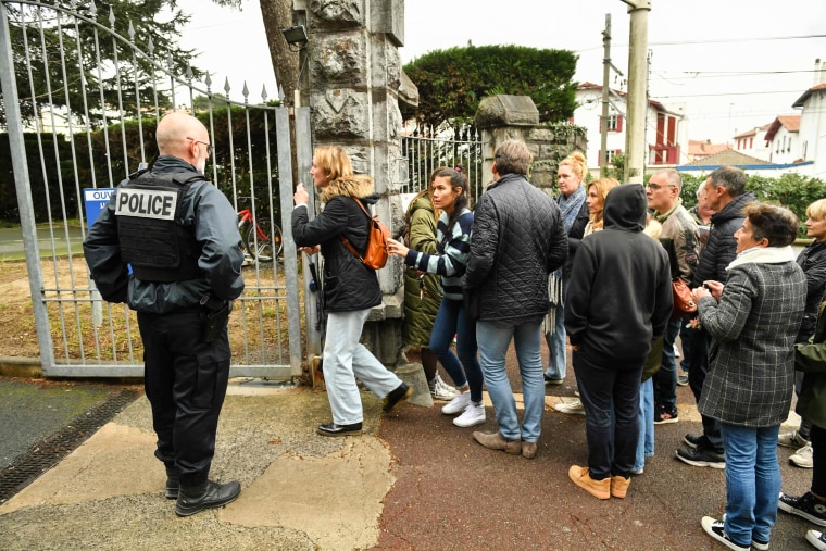 Onlookers gather at the entrance of a school where a teacher died after being stabbed by a student in Saint-Jean-de-Luz, France, on Feb. 22, 2023.