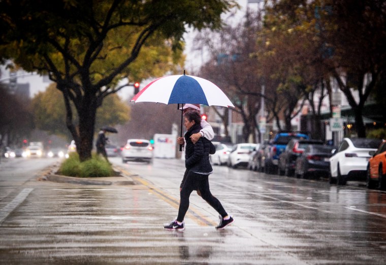 Pedestrians walk across the street amidst heavy rain in Pasadena, Calif.