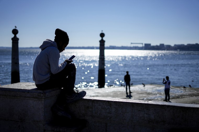 A young man checks his phone by the Tagus river at Lisbon's Comercio square on Jan. 30, 2023.
