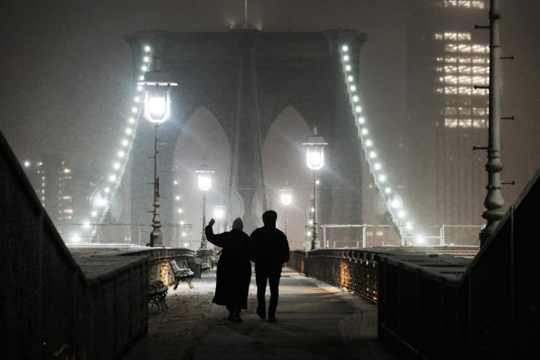 Snow falls as people walk across the Brooklyn Bridge in New York City on Monday night.