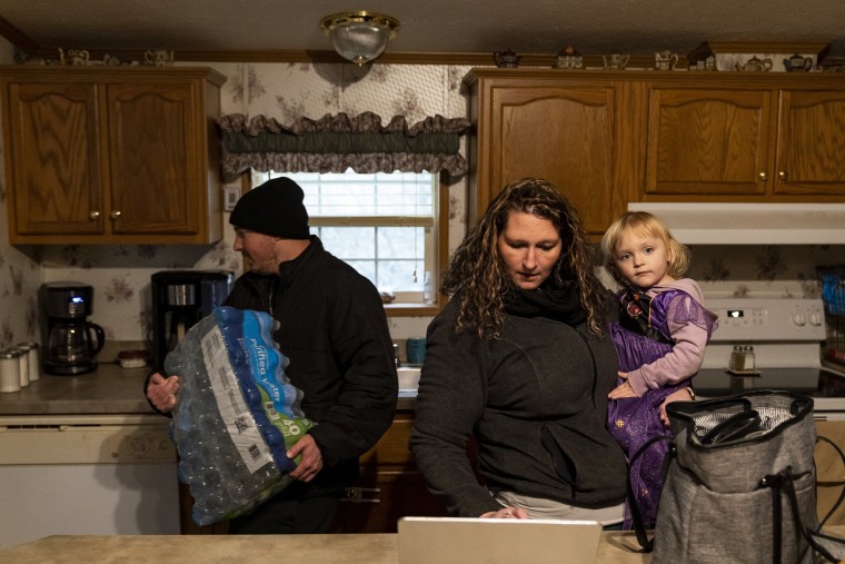 Joshua Barber carries a case of water into his house after returning from a donation bank in East Palestine, Ohio while his sister, Jessica Fosnaught, works on her computer on Feb. 17, 2023 in Darlington, Penn.