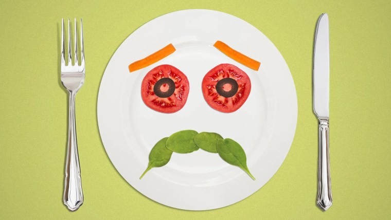 Ilustración de un mantel de color verde sobre el cual hay un tenedor, un cuchillo y un plato de color blanco. En el plato hay jitomate, espinaca y zanahora haciendo la forma de una carita triste :( en representación de mala alimentación