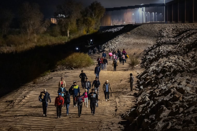Inmigrantes caminan a lo largo de la barrera fronteriza entre Estados Unidos y México el 30 de diciembre de 2022 en Yuma, Arizona.
