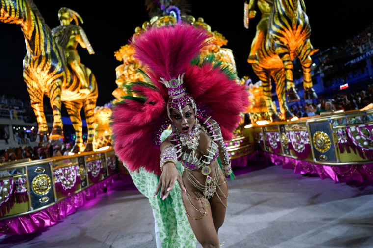 Una mujer afrobrasileña con estocado de plumas color rosa y un bikini con motivos de garras y tonos azul y jade desfila frente a carros alegóricos con zebras de papel maché durante el Carnaval de Río de Janeiro 2023