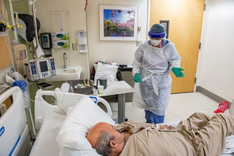 Una doctora con equipo de protección personal se acerca a un paciente de edad avanzada en un cuarto de hospital