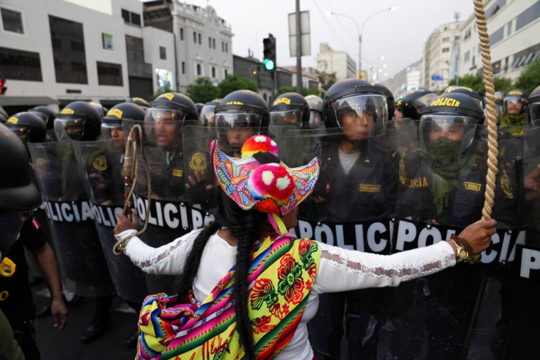 Una mujer con vestimenta andina como un sombrero tongo de muchos colores se ve de espaldas. Está encarando a una fila de decenas de policías en vestimenta antidisturbios durante una protesta en Lima, Perú, el 9 de febrero de 2023