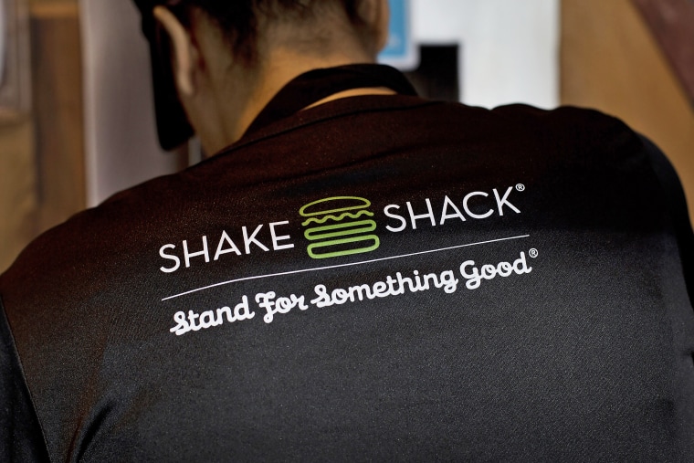 An employee is seen wearing a branded t-shirt while cleaning a table at a Shake Shack.