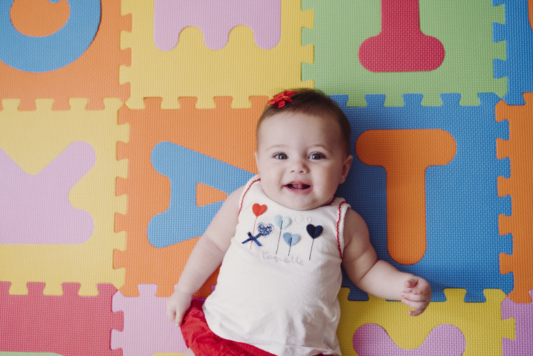 Cute baby girl relaxing on colorful alphabetical puzzle playmat at home