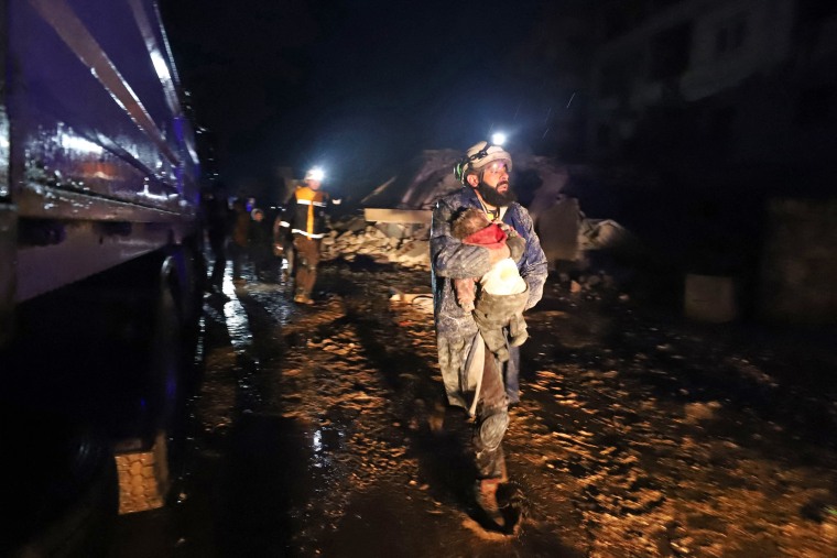 A member of the Syrian civil defense, known as the "White Helmets," carries a child rescued from the rubble in Zardana in Syria' Idlib province, early on Feb. 6, 2023. 
