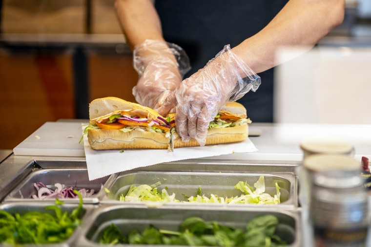 An employee halves a Subway sandwich at a Subway restaurant.