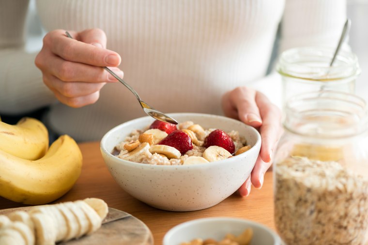 Woman putting together oatmeal with banana, strawberries and nuts.