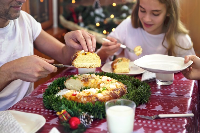 Family sitting at the table, father serving slices of a roscón de reyes (king cake).