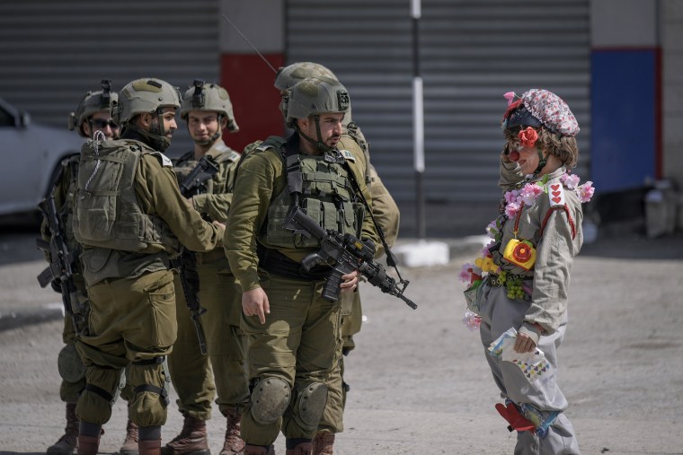 Un activista israelí vestido de payaso saluda a un grupo de soldados israelíes durante una manifestación de solidaridad organizada por activistas israelíes de izquierda en la ciudad de Hawara, en Cisjordania, el 3 de marzo de 2023.