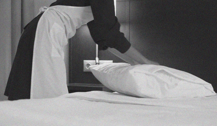 A member of the house cleaning staff makes a bed in a hotel room.