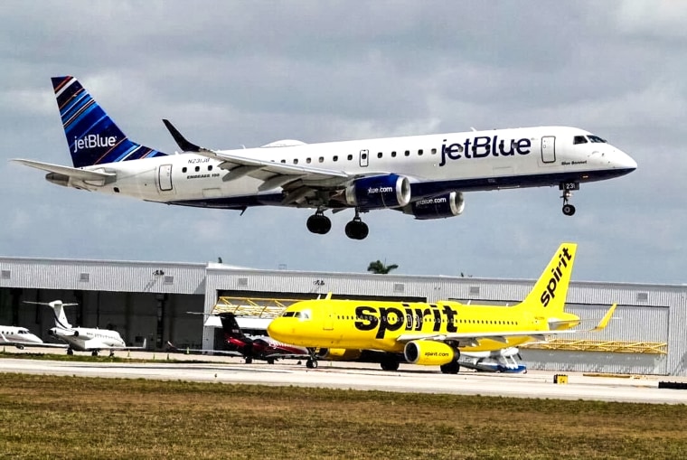 A JetBlue airliner lands past a Spirit Airlines jet on taxi way at Fort Lauderdale Hollywood International Airport on April 25, 2022, in Florida.