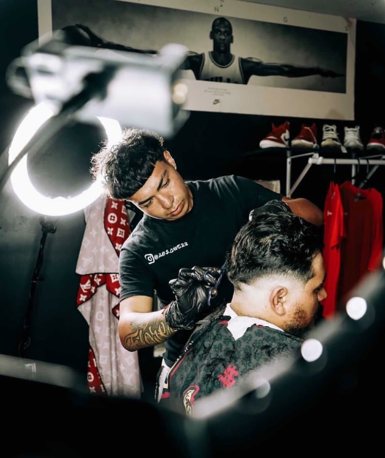 Image: Carlos Flores, a barber, cuts the hair of another man.