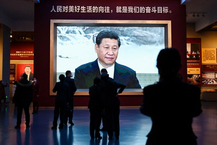 People walk past a video screen showing a speech by Chinese President Xi Jinping at the Museum of the Communist Party of China in Beijing on March 3, 2023.