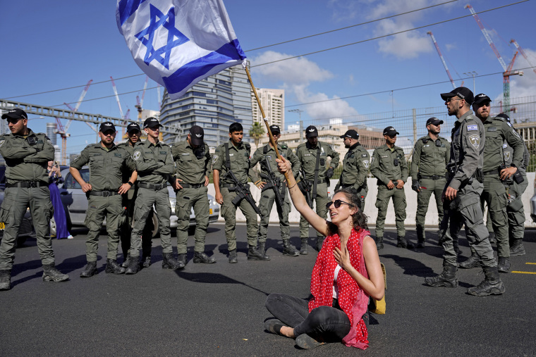 A demonstrator waves the Israeli flag Thursday in front of paramilitary border police in Tel Aviv during a protest against plans to overhaul the judicial system.