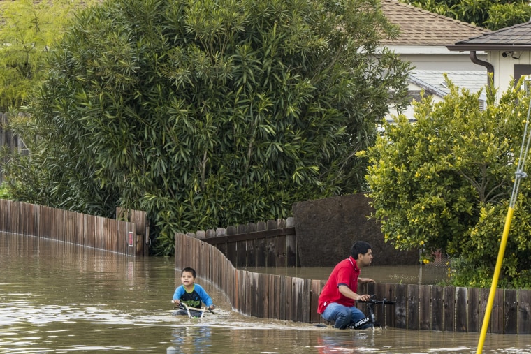 A boy and a man ride bicycles through floodwaters in Watsonville, Calif., on March 11, 2023.