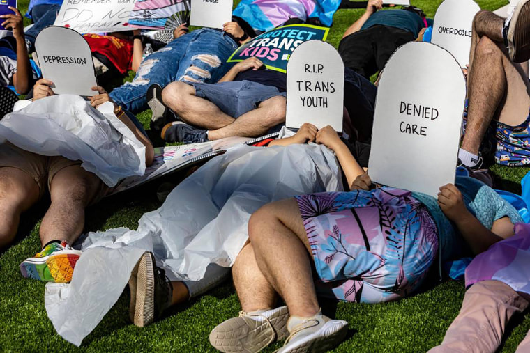 Protesters lie on the ground holding cardboard signs shaped like tombstones in front of the Marriott Fort Lauderdale Airport as the Florida Board of Medicine meets inside.