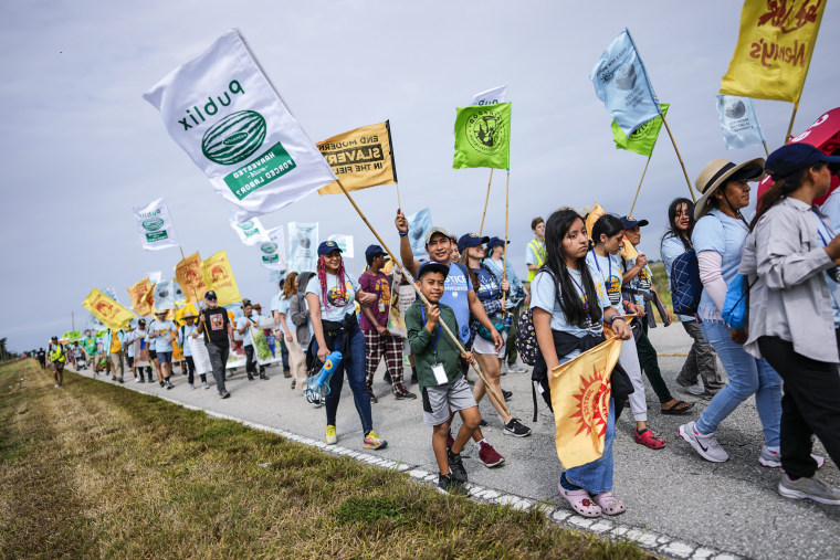 Image: Gelder Perez, 10, center, carries a protest flag as he walks with his uncle Leonel Perez, center right, on the first day of a five-day trek aimed at highlighting the Fair Food Program, in an effort to pressure retailers to leverage their purchasing power to improve conditions for farmworkers, on March 14, 2023, in Pahokee, Fla.