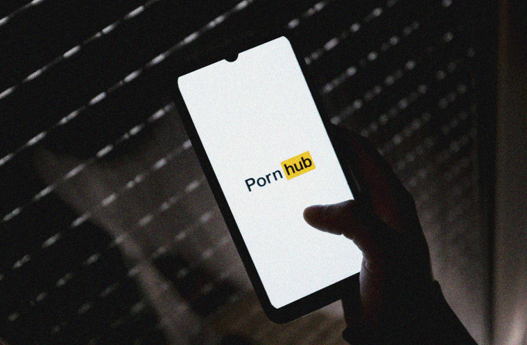 Image: The Pornhub logo on a phone screen in a dark room.