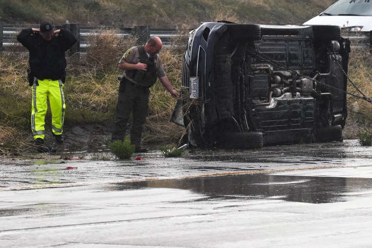 Emergency personnel look at a vehicle that flipped during a storm 