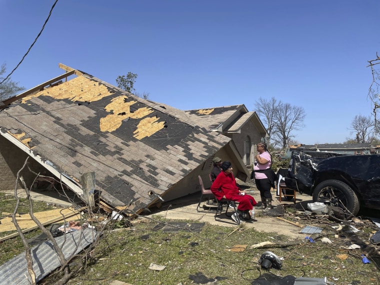 People sit in front of a damaged home in Silver City, Miss.