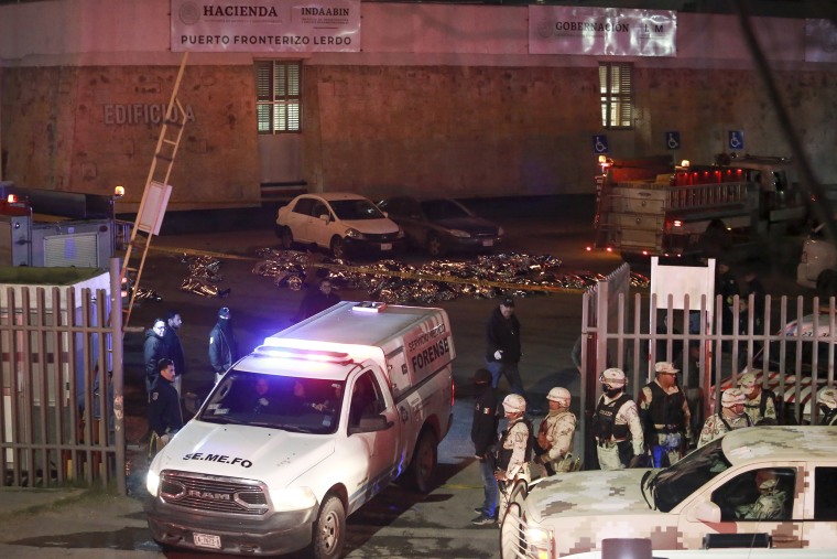 The bodies of migrants lie covered on the ground, behind, after a deadly fire broke out at an immigration detention center in Ciudad Juarez, Mexico, Tuesday, March 28, 2023.