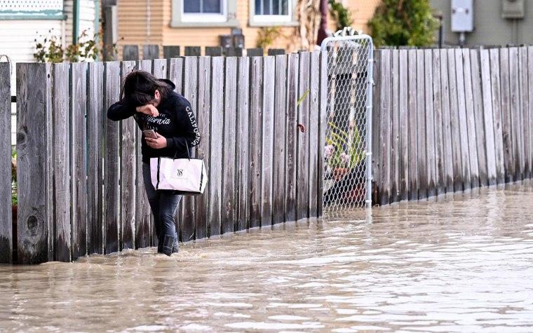 A resident treads through flood waters to reach her home in Pajaro, Calif., on March 11, 2023.
