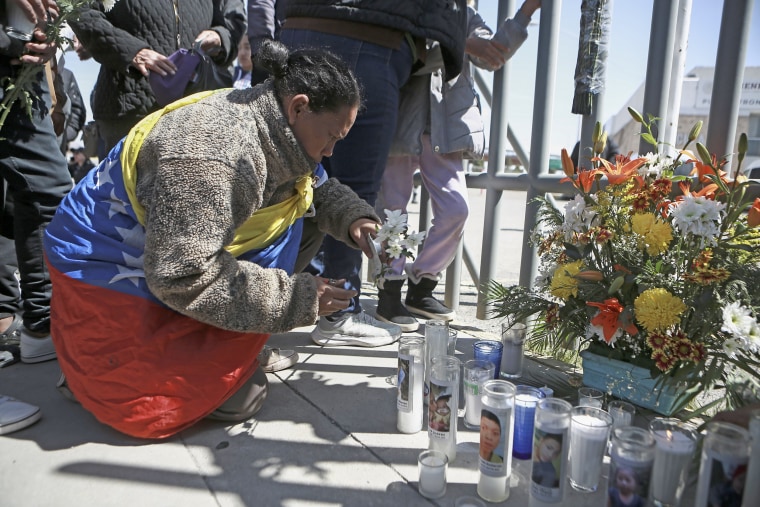A woman places flowers in front of a gate that has been converted into a memorial outside a Mexican immigration detention center 