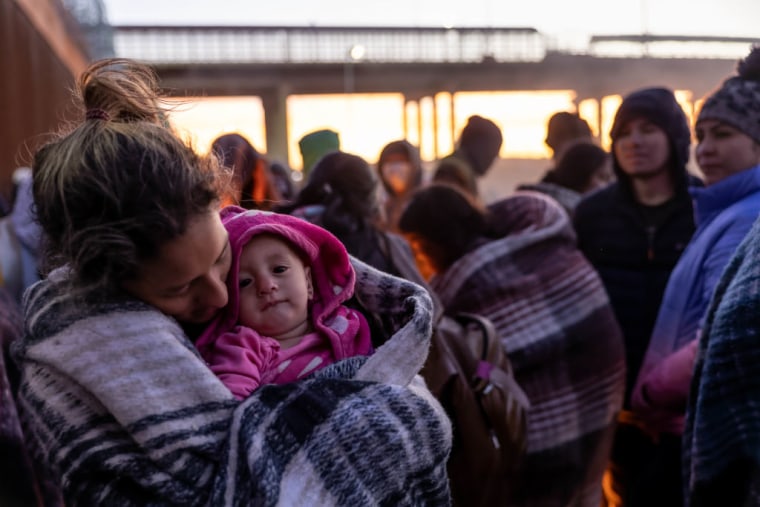 Una inmigrante venezolana sostiene a su hija de 10 meses, junto a la valla fronteriza entre Estados Unidos y México el 22 de diciembre de 2022 en El Paso, Texas.