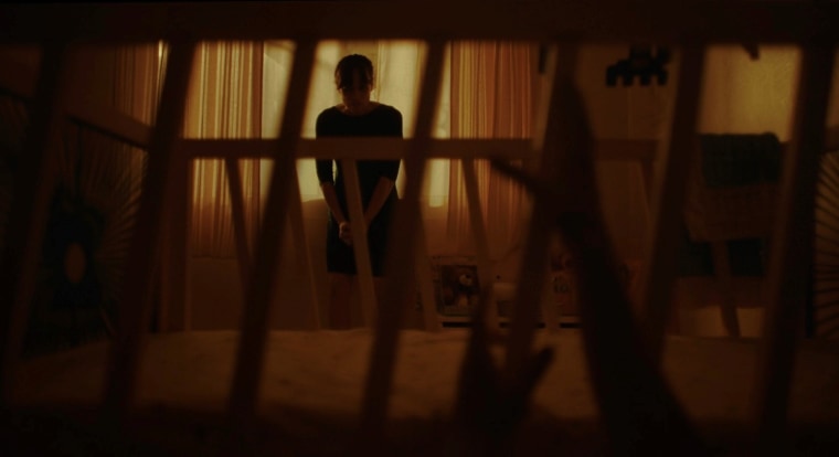 Una toma de la película de terror "Huesera/The Bone Woman", de Michelle Garza Cervera muestra a una mujer contra una ventana. Frente a ella hay una cuna y dos manos saliendo del piso agarrando la cuna