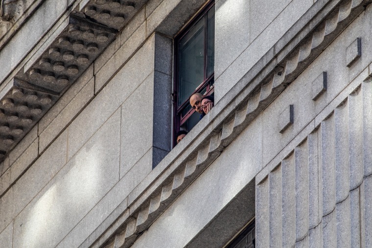 People look out from the State Office Building at the assembled media and police below ahead of former President Donald Trump’s arraignment in New York on April 4, 2023.