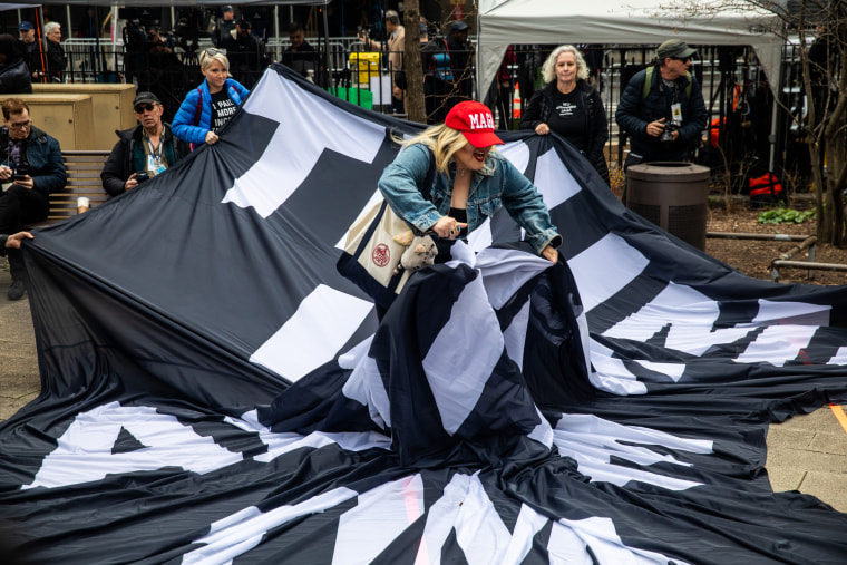 A Trump supporter tries to tear a banner that reads “Trump lies all the time” outside New York Criminal Court ahead of the former president's arraignment.