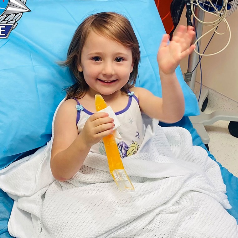In this photo provided by the Western Australia Police, four-year-old Cleo Smith waves as she sits on a bed in hospital, Wednesday, Nov. 3, 2021, in Carnarvon, western Australia. Police smashed their way into a suburban house on Wednesday and rescued Cleo whose disappearance from her family's camping tent on Australia's remote west coast more than two weeks ago both horrified and captivated the nation. The seal of Western Australia Police is seen at top left. (Western Australia Police via AP)