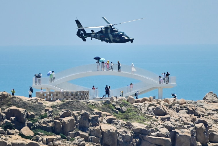 Tourists look on as a Chinese military helicopter flies past China's Pingtan Island, the closest point to Taiwan, on Aug. 4, 2022, ahead of massive military drills.