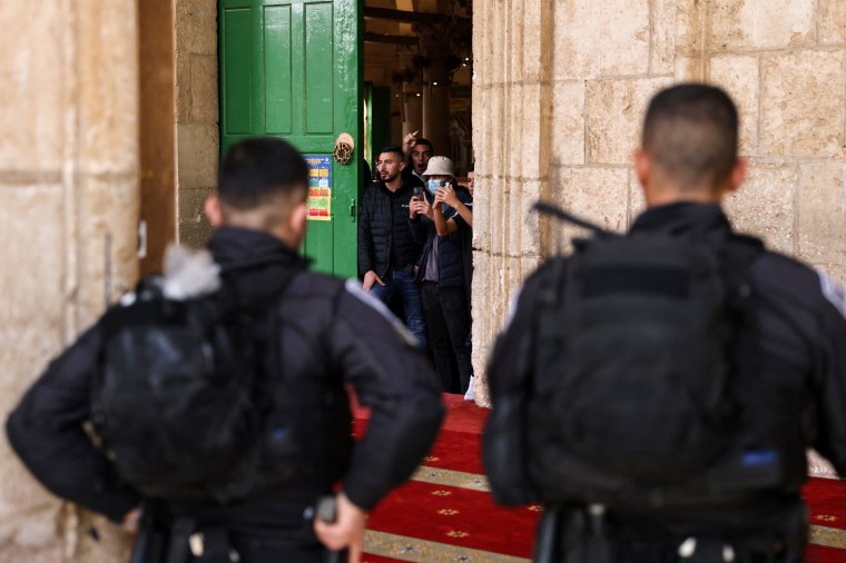 Palestinians stand inside the Al-Aqsa mosque as Israeli security forces watch in Jerusalem on April 9, 2023.