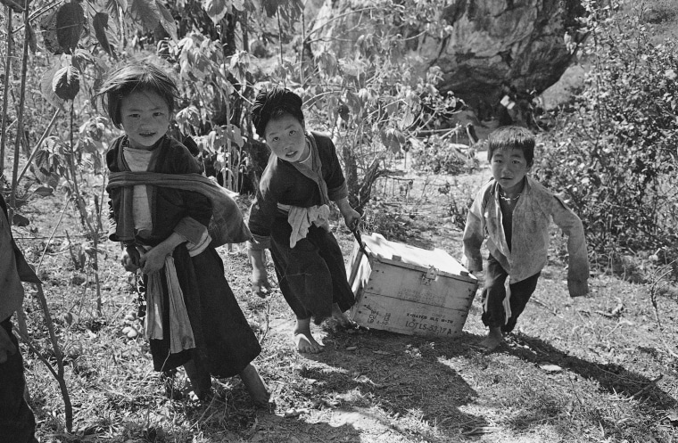 Meo children drag an ammunition box filled with personal belongings up a hill in Laos