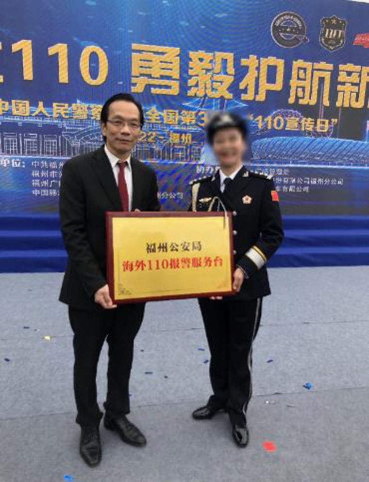 Lu Jianwang stands with an official  of China's Ministry of Public Security holding a sign which reads “Fuzhou Public Security Bureau, Overseas 110 Report to Police Service Station," during a ceremony in Fuzhou, China in January 2022.