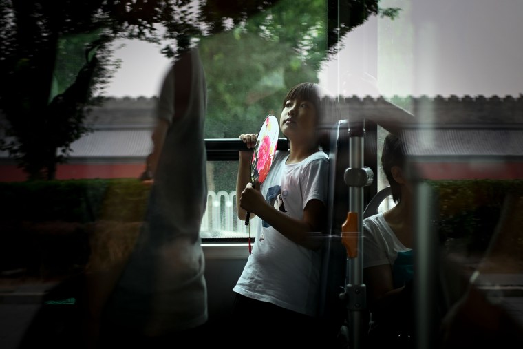A girl holds fan while riding a bus during a summer day in Beijing