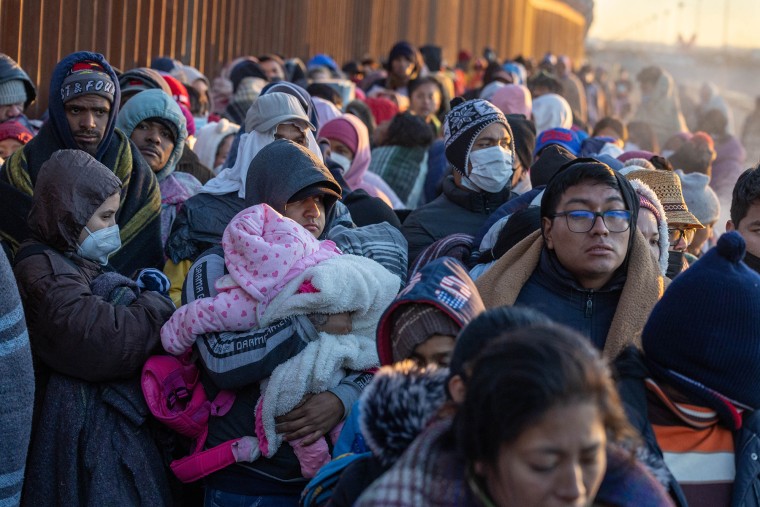 Los inmigrantes se abrigan contra el frío después de pasar la noche acampados junto a la valla fronteriza entre Estados Unidos y México el 22 de diciembre de 2022 en El Paso, Texas.
