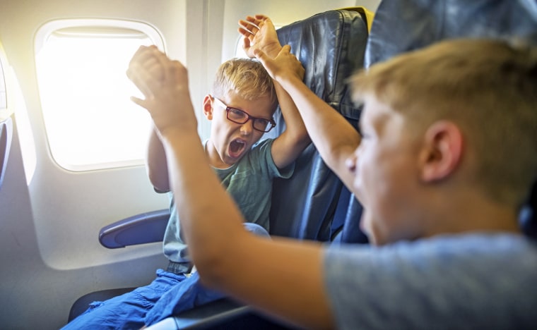 Two loud and mischievous boys fighting and yelling on a plane.
