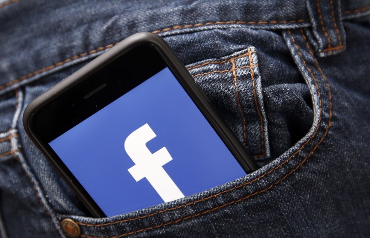 Facebook logo is seen on the screen of an iPhone pocking out of a pocket.
