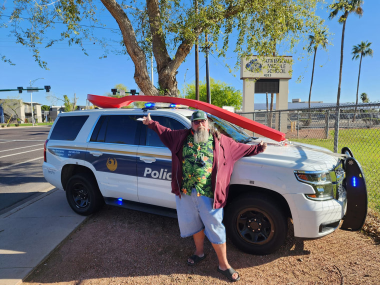 Michael Foster posing in front of the spoon affixed to the front of a police cruiser.