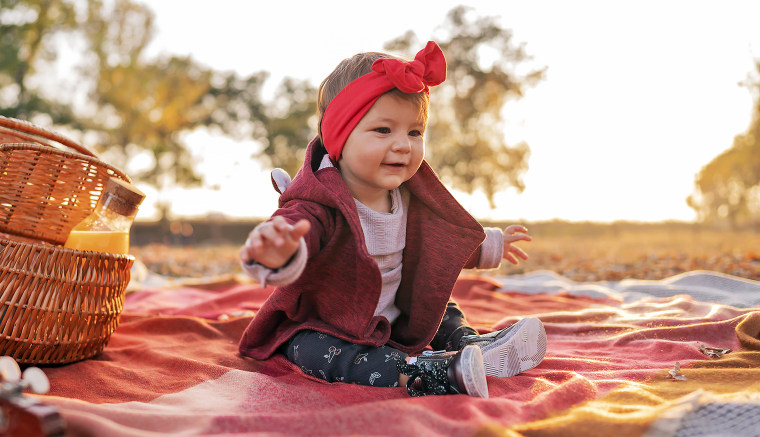 Portrait of a cute baby girl sitting on a picnic blanket outdoors.
