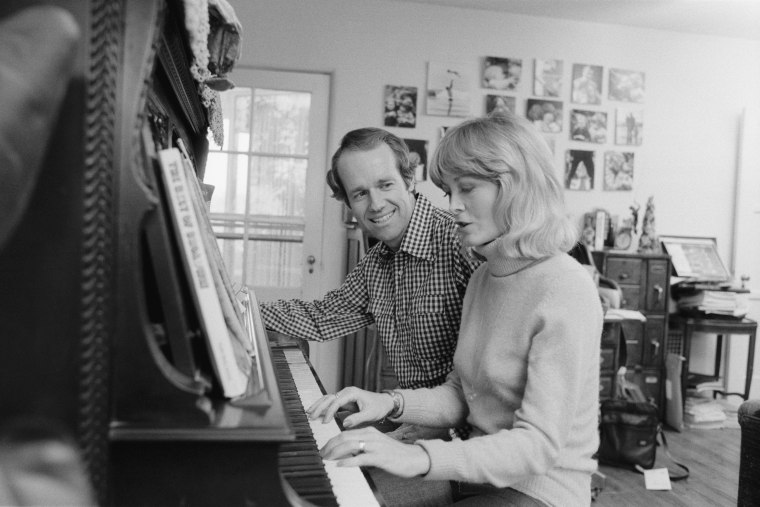 Mike and Judy Farrell play piano at home in a black and white photo