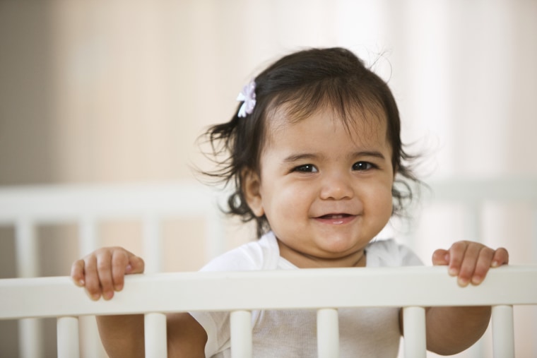 Hispanic baby girl standing in crib